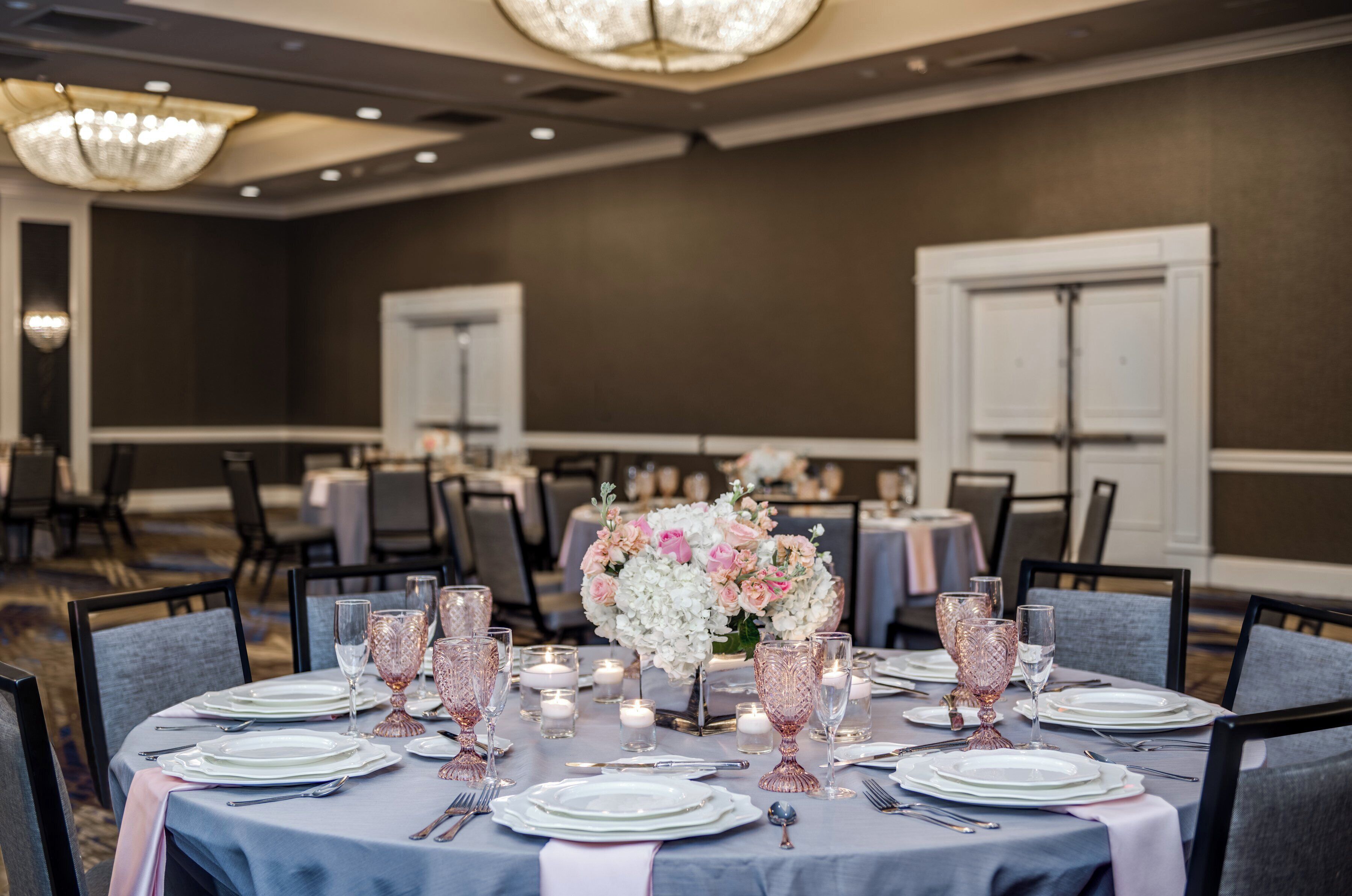 Une table de banquet dressée pour un événement formel, agrémentée d’un centre de table floral, de bougeoirs et de porcelaine de qualité.