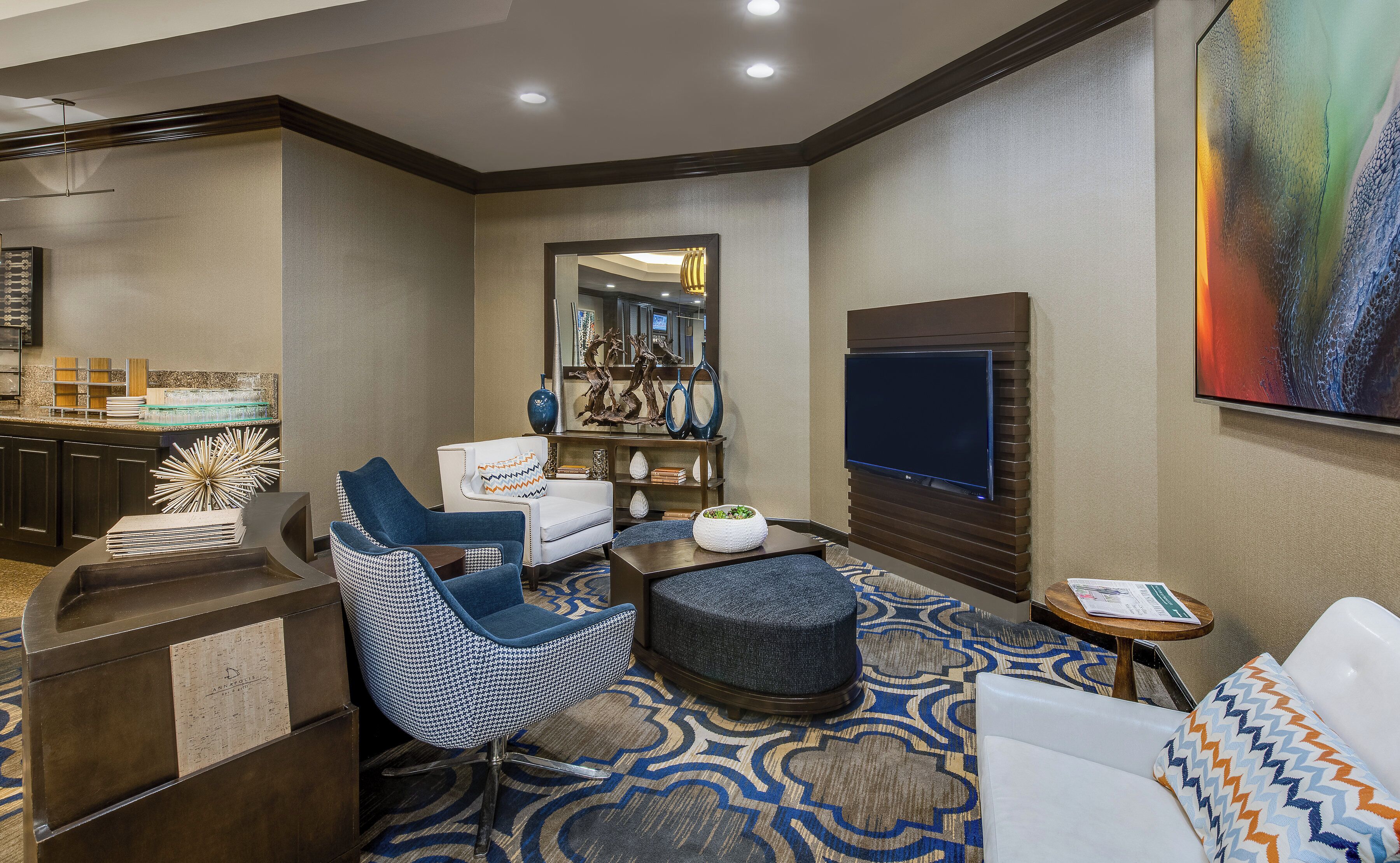 A hotel room with a seating area, a television, a large painting, and a minibar.