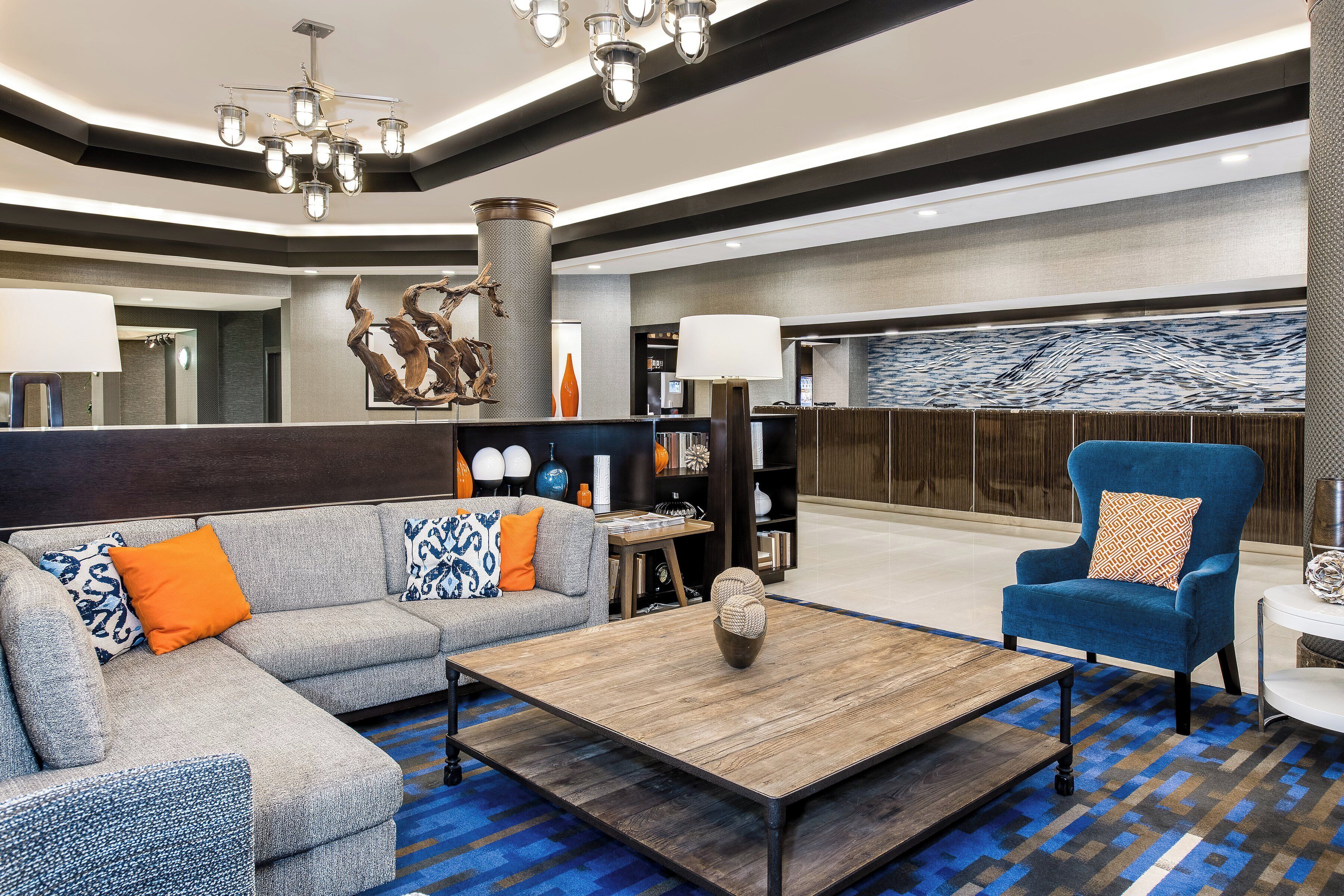 Un hall d’entrée moderne avec un canapé d’angle, un fauteuil bleu, une table basse et un élément décoratif mural.