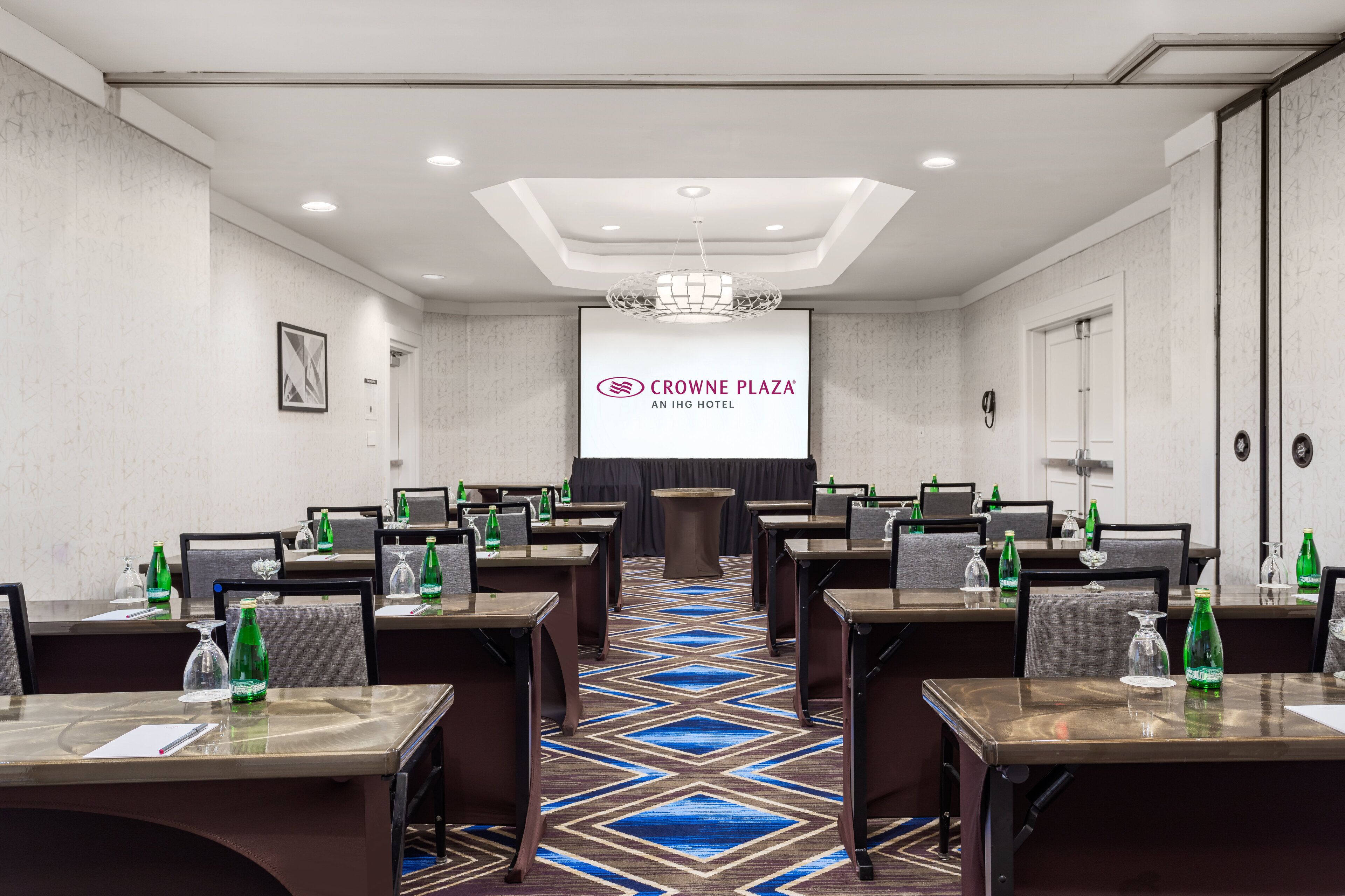 A conference room with tables, chairs, and a projector screen displaying the hotel's name.