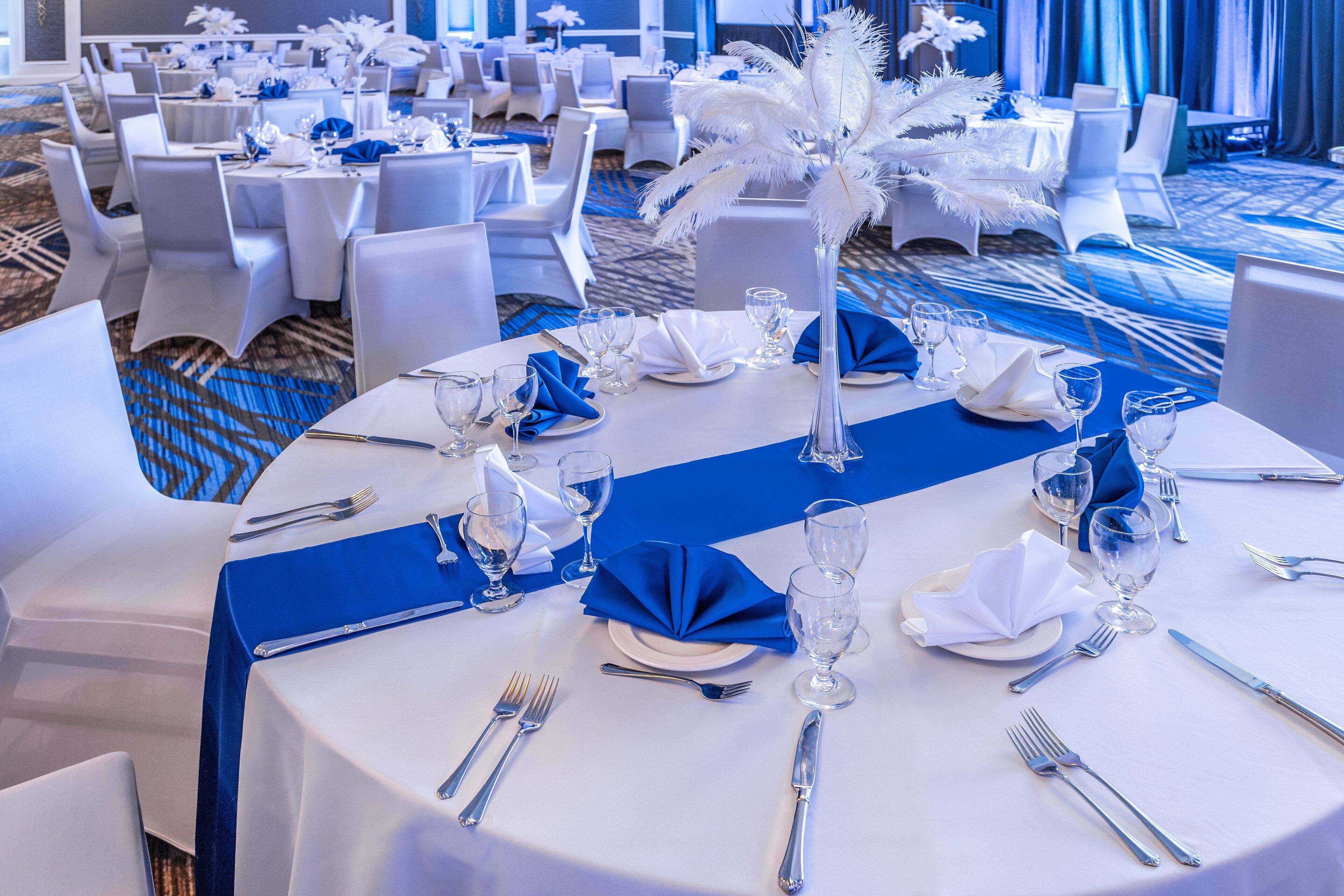 A banquet hall with round tables set for dining, white chairs, and a blue table runner.