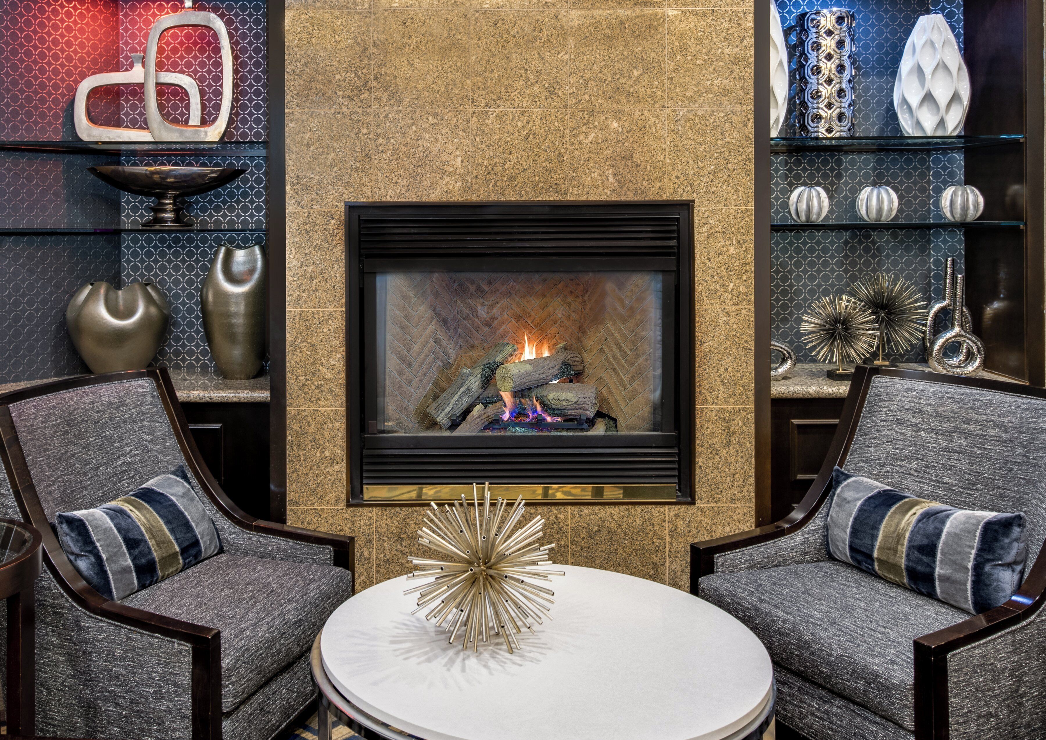 A modern living room with a fireplace, two armchairs, a coffee table, and decorative items.