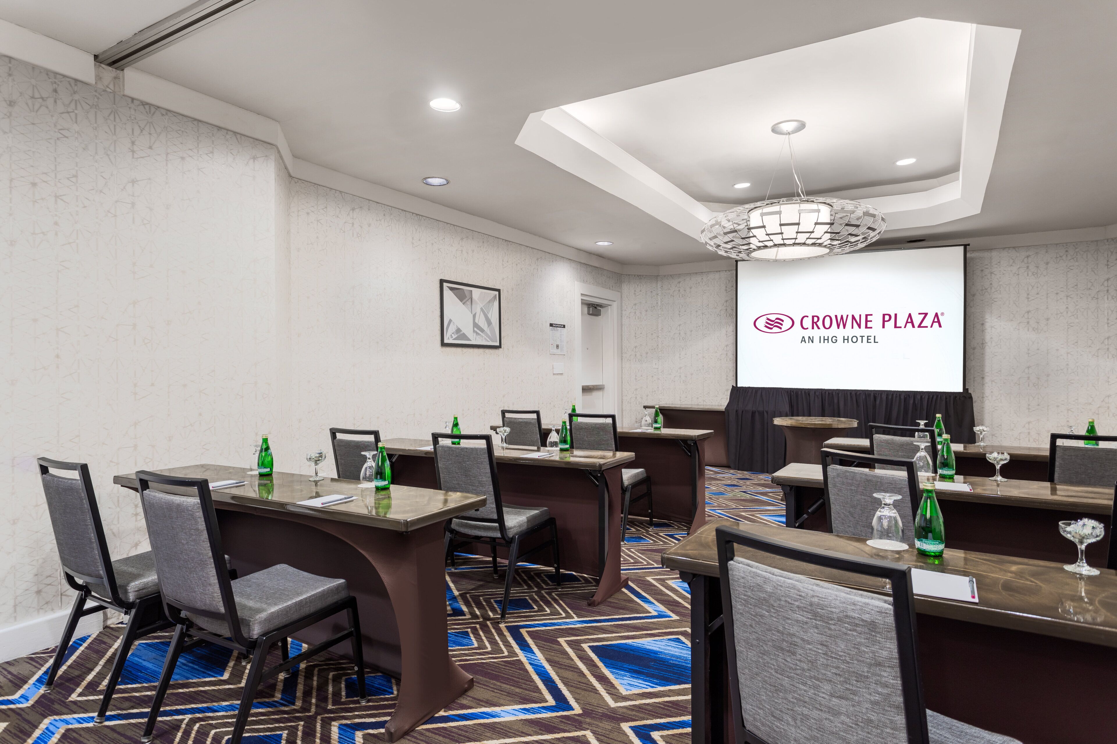 A conference room with tables, chairs, and a projector screen displaying the hotel's name.