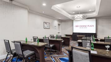 A conference room with tables, chairs, and a projector screen displaying the hotel's name.