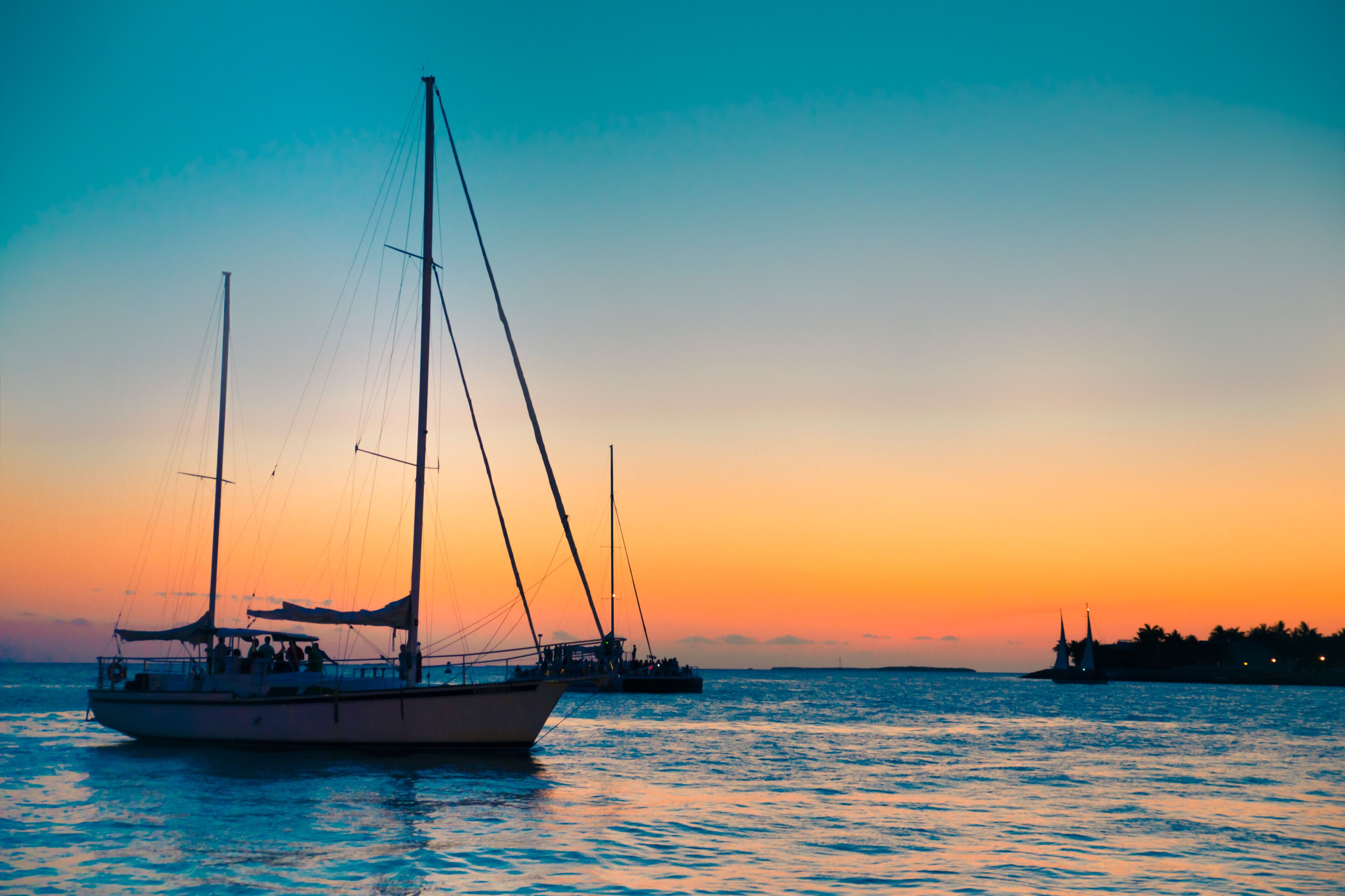 A boat with a mast and sails on calm water during sunset.
