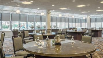 A hotel conference room with round tables, chairs, and a large window providing a view of the outdoors.