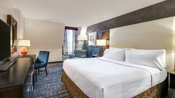 Ein Hotelzimmer mit einem großen Bett, einem Schreibtisch mit Stuhl, einem Fernseher und zwei Lampen.
