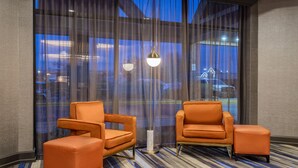 A hotel room with two orange armchairs, a floor lamp, and large windows with a view of a parking lot. - Crowne Plaza Annapolis by IHG (Annapolis)