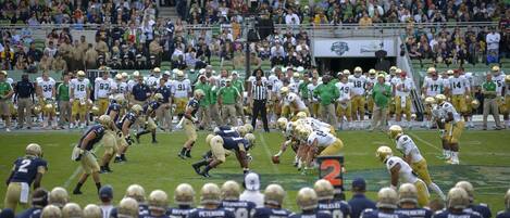 A football stadium with multiple teams on the field, spectators in the stands, and a scoreboard.