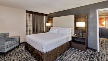 A hotel room with a large bed, a bedside table with a lamp, a chair, and a view of the hallway.