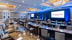 A conference room with long tables, chairs, and a large screen displaying the Crowne Plaza logo. - Crowne Plaza Annapolis by IHG (Annapolis)