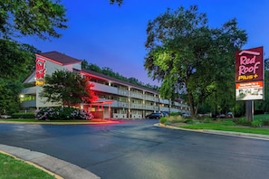 Un motel con letrero de techo rojo, varios espacios de estacionamiento y un césped bien cuidado.