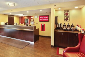 A hotel reception area with a reception desk, a clock, a sign indicating free Wi-Fi, and a coffee station with various beverages. - Red Roof Inn PLUS+ Washington DC - Alexandria  (Alexandria)