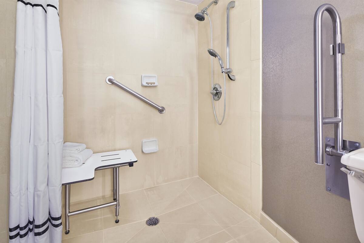 Ein Badezimmer mit Dusche, Haltegriffen, einem weißen Waschbecken und einer Toilette.