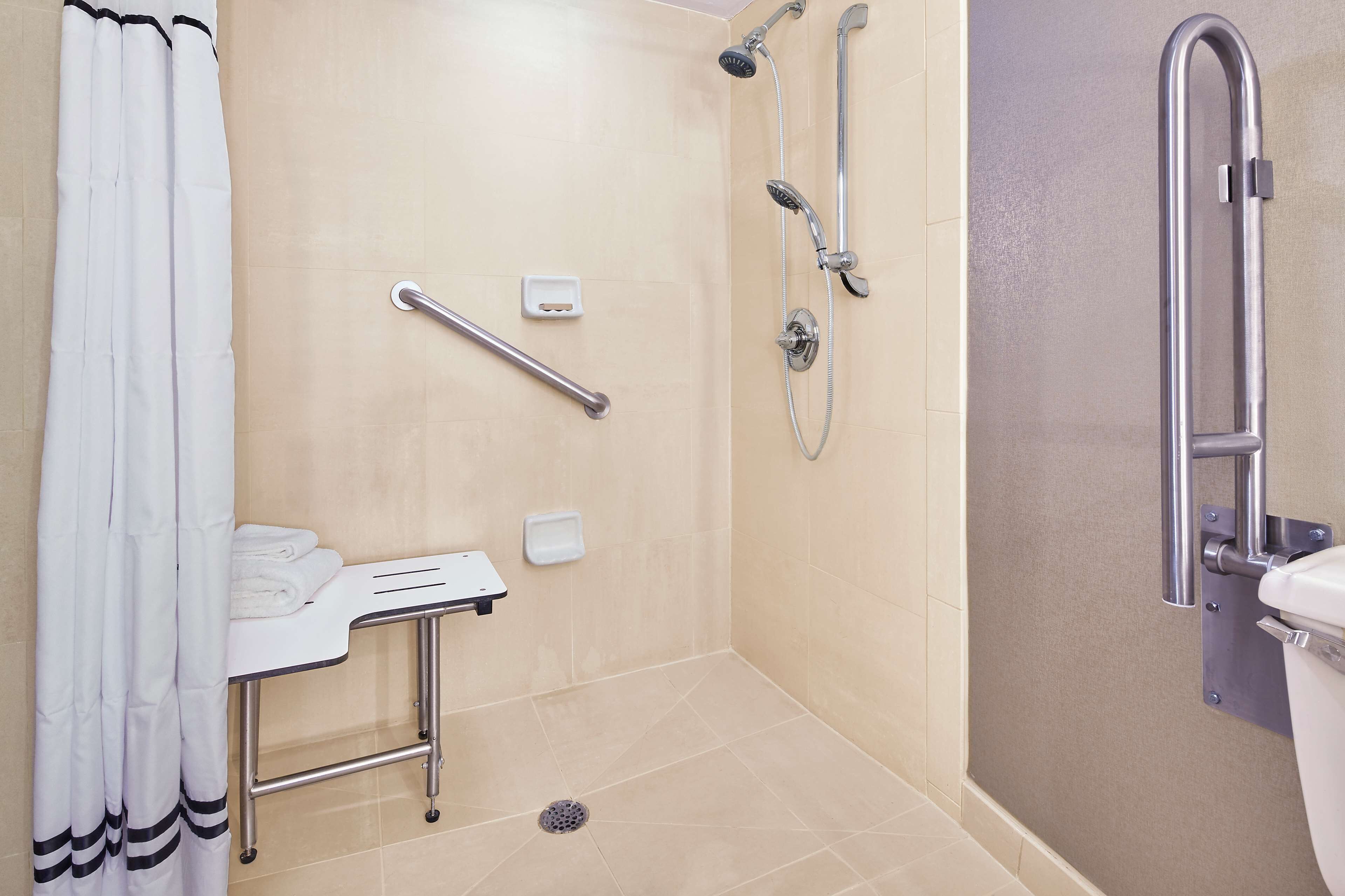 Une salle de bain équipée d’une douche, de toilettes, d’une barre d’appui et d’un lavabo avec un porte-serviettes.