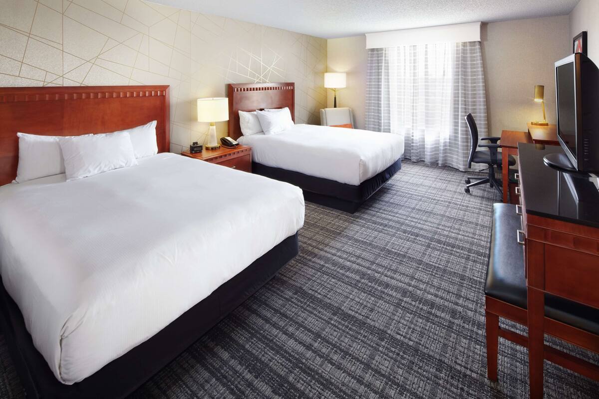 Ein Hotelzimmer mit zwei Betten, einem Schreibtisch, einem Fernseher, einem Stuhl und einer Lampe.