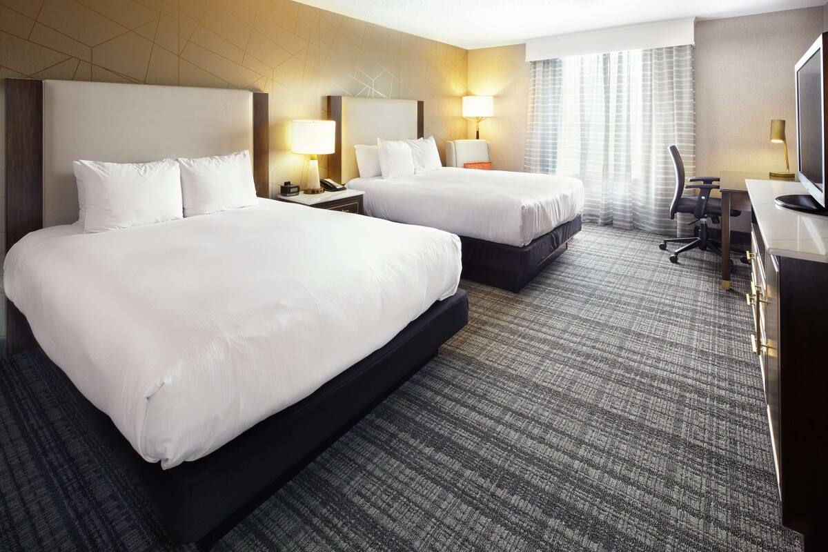 Ein Hotelzimmer mit zwei Betten, einem Schreibtisch, einem Stuhl und einem Fernseher.
