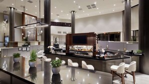 A modern hotel lobby with a central bar area, seating, and a large screen. - DoubleTree by Hilton Dallas Near the Galleria (Dallas)