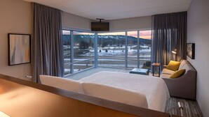 A hotel room with a large bed, a sofa, a desk, and a view of a snowy landscape. - DoubleTree by Hilton Dallas Near the Galleria (Dallas)