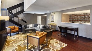 A modern living room with a staircase, a sectional sofa, a coffee table, and a desk with a chair. - DoubleTree by Hilton Dallas Near the Galleria (Dallas)