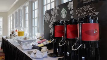 A coffee station with multiple coffee dispensers, a buffet table with various food items, and a backdrop with a Starbucks logo and floral design.