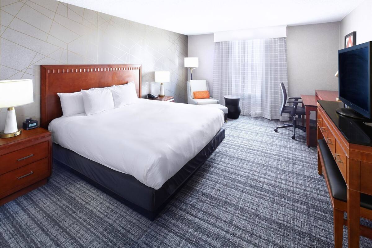 A hotel room with a large bed, bedside tables with lamps, a desk with a chair, and a television.