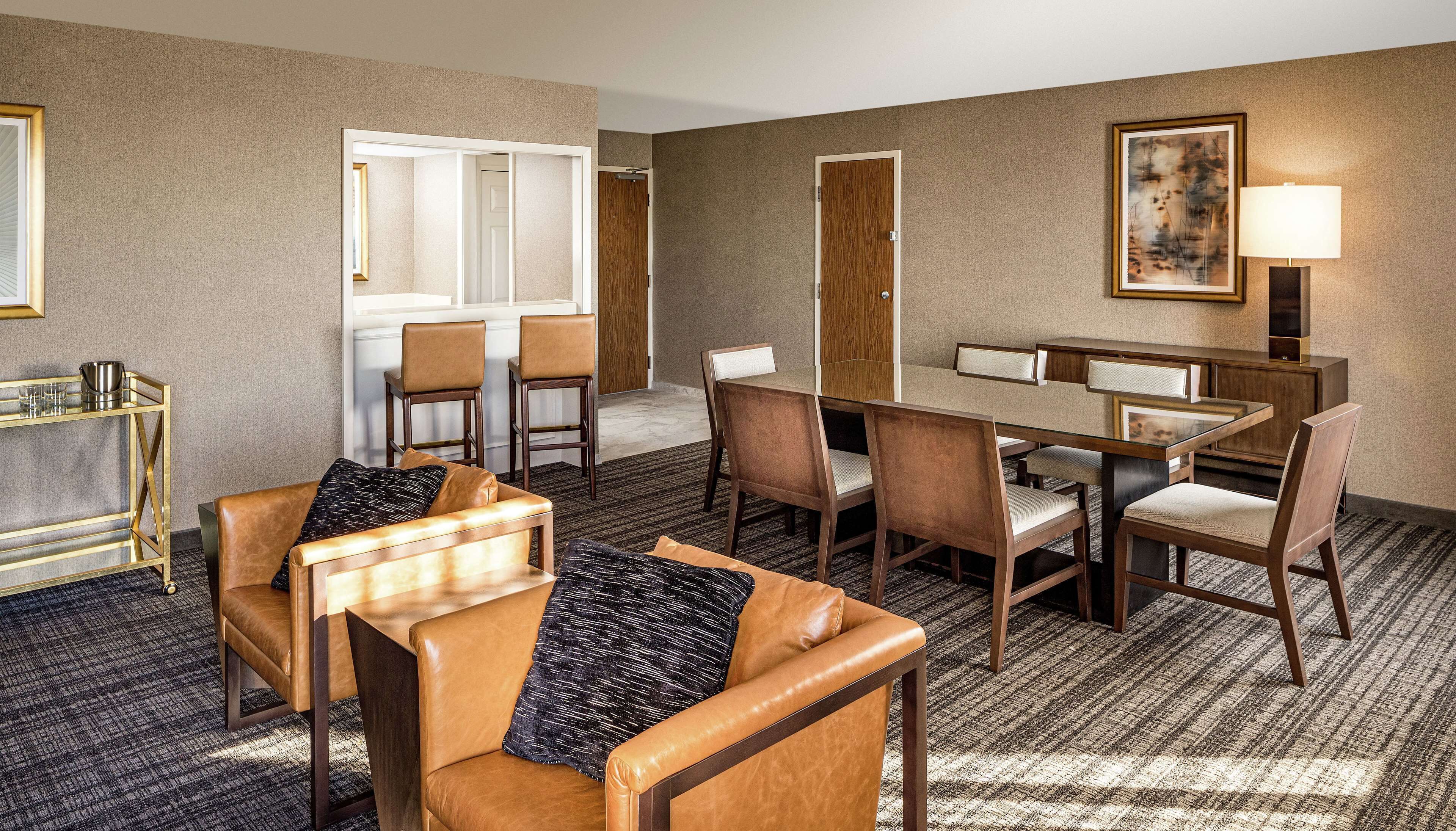 A hotel room with a dining area, a sofa set, and a lamp.