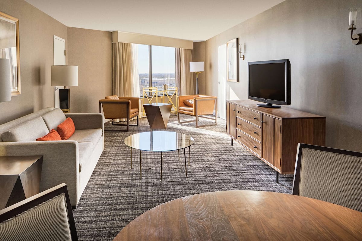 Ein Hotelzimmer mit Sofa, Sessel, Couchtisch, Fernseher und Blick auf die Stadt.
