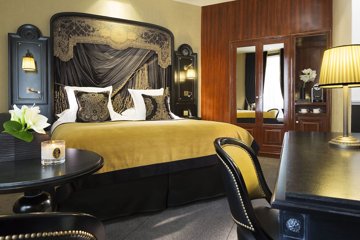 A hotel room with a large bed, a round table, a chair, a lamp, and a mirror.