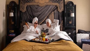 Un dormitorio lujoso con una cama grande, cabecera ornamentada y una bandeja con alimentos para el desayuno.