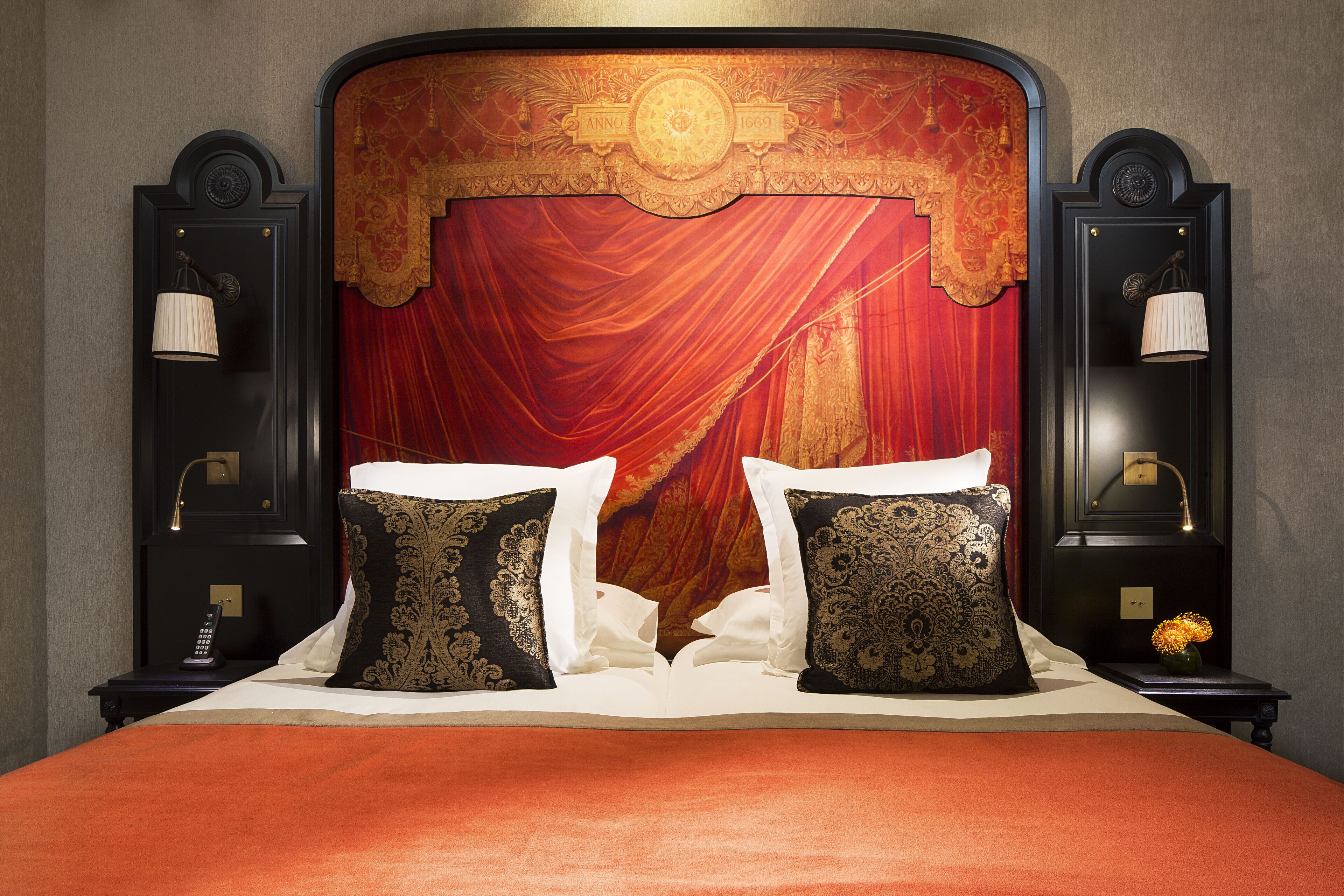 A bed with red curtains, two black and gold pillows, and a nightstand with a lamp.