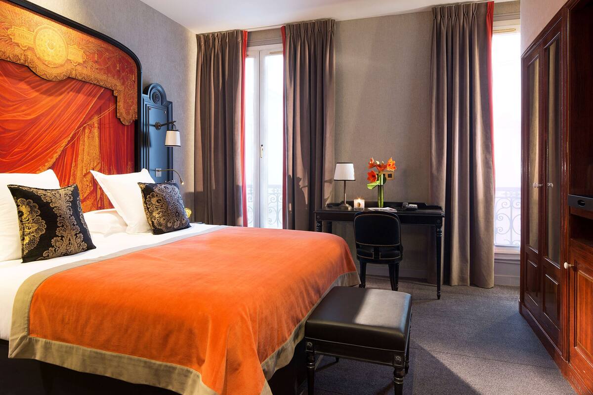 A hotel room with a large bed, a desk, a chair, and a wardrobe.