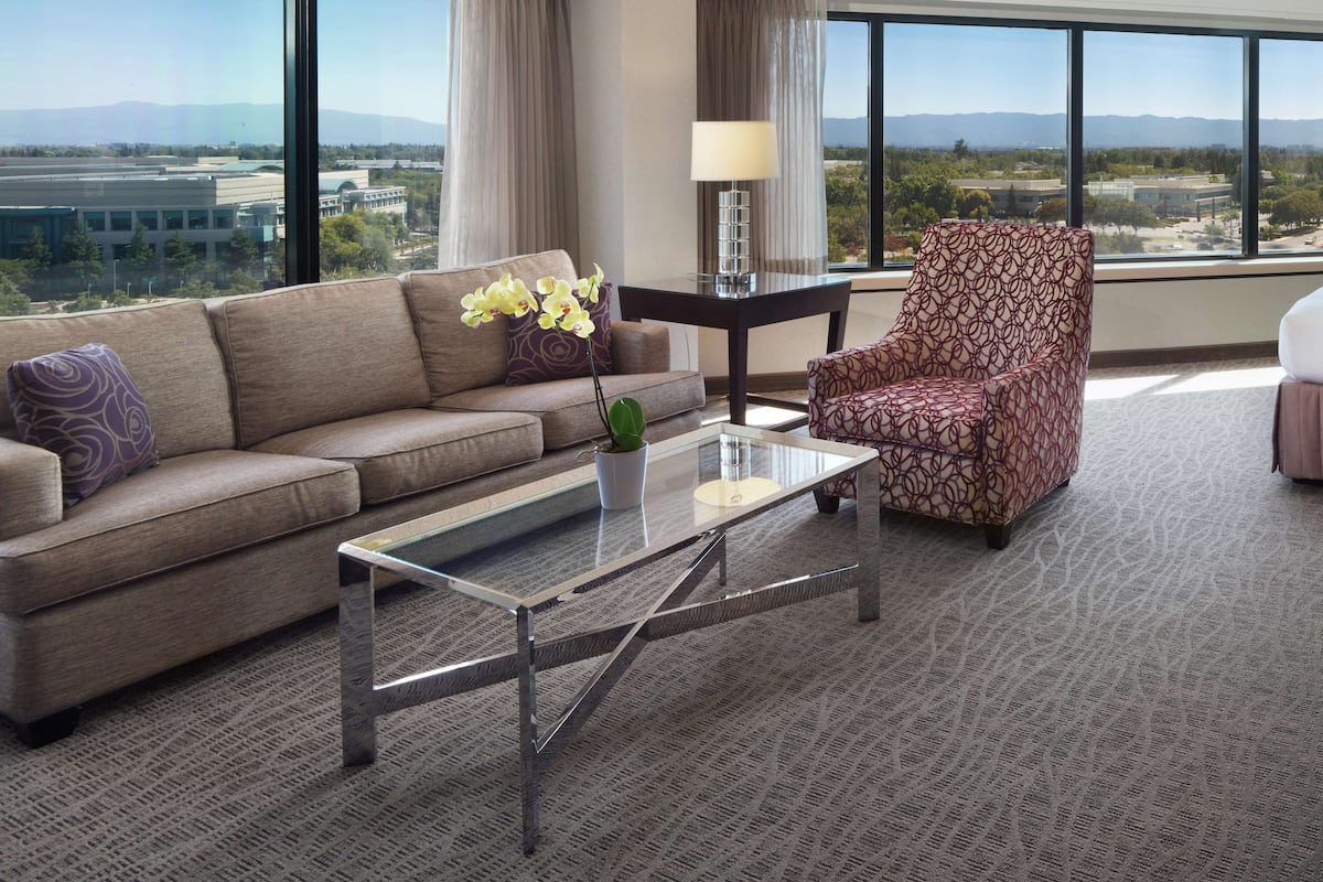 A modern hotel room with a sofa, armchair, and a glass coffee table.