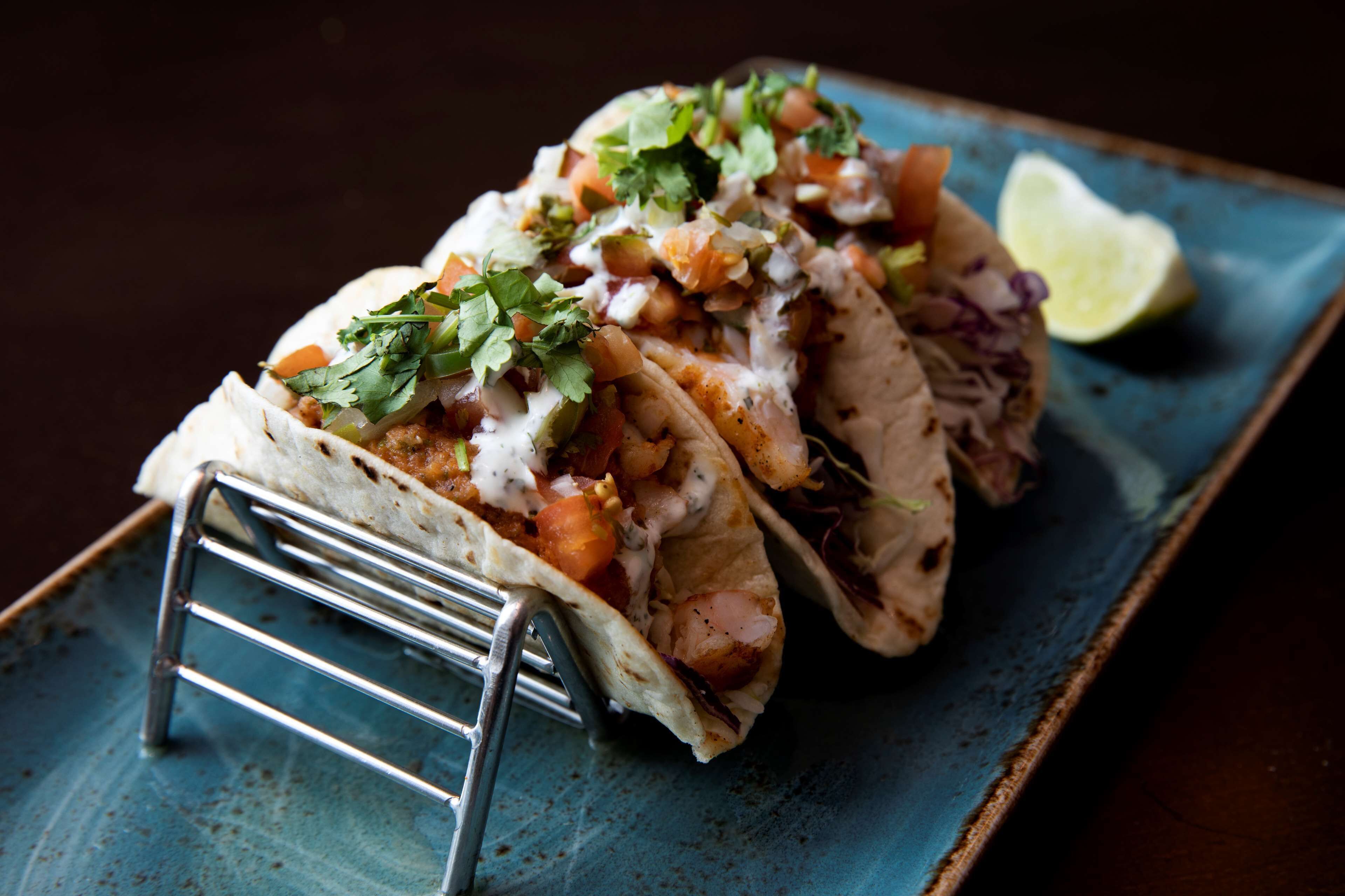 Três tacos em um prato azul com uma fatia de limão.