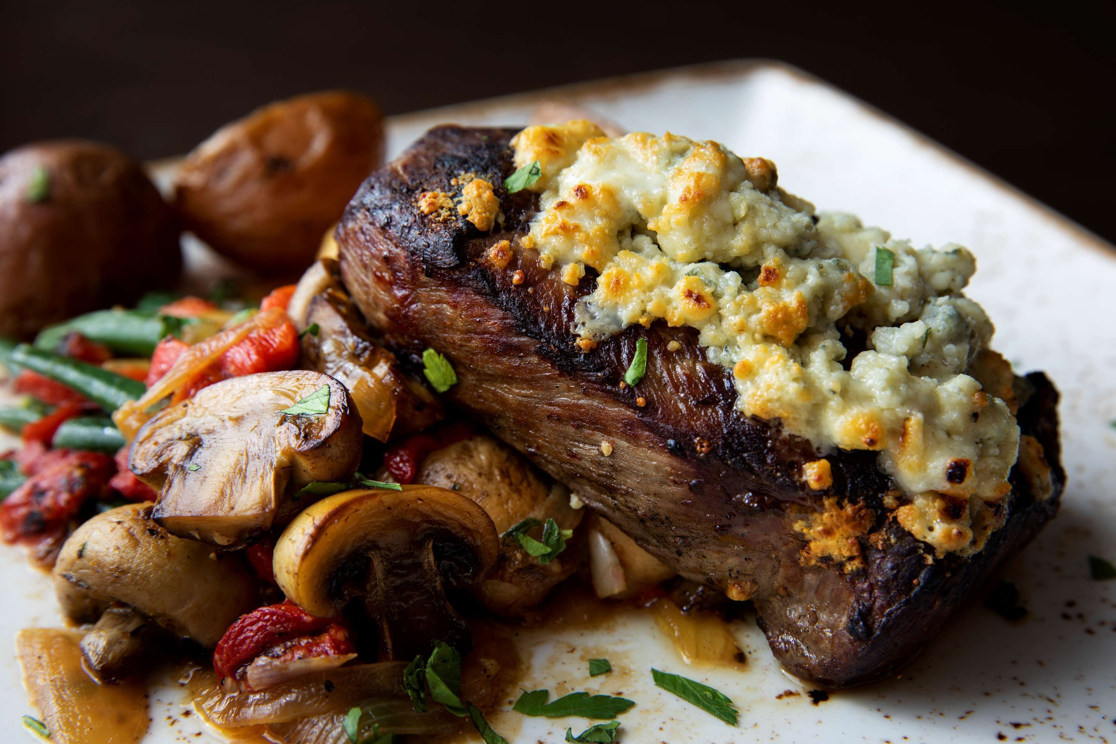 A steak with a creamy topping and roasted vegetables on a plate.