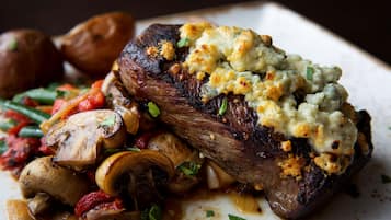 A steak with a creamy topping and roasted vegetables on a plate.