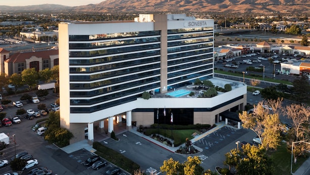 A multi-story hotel with a pool on the rooftop, surrounded by a parking lot and a mountainous backdrop. - Sonesta San Jose - Milpitas (Milpitas)