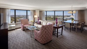 A hotel room with a large window, a sofa, a chair, a small table, and a dining area. - Sonesta San Jose - Milpitas (Milpitas)