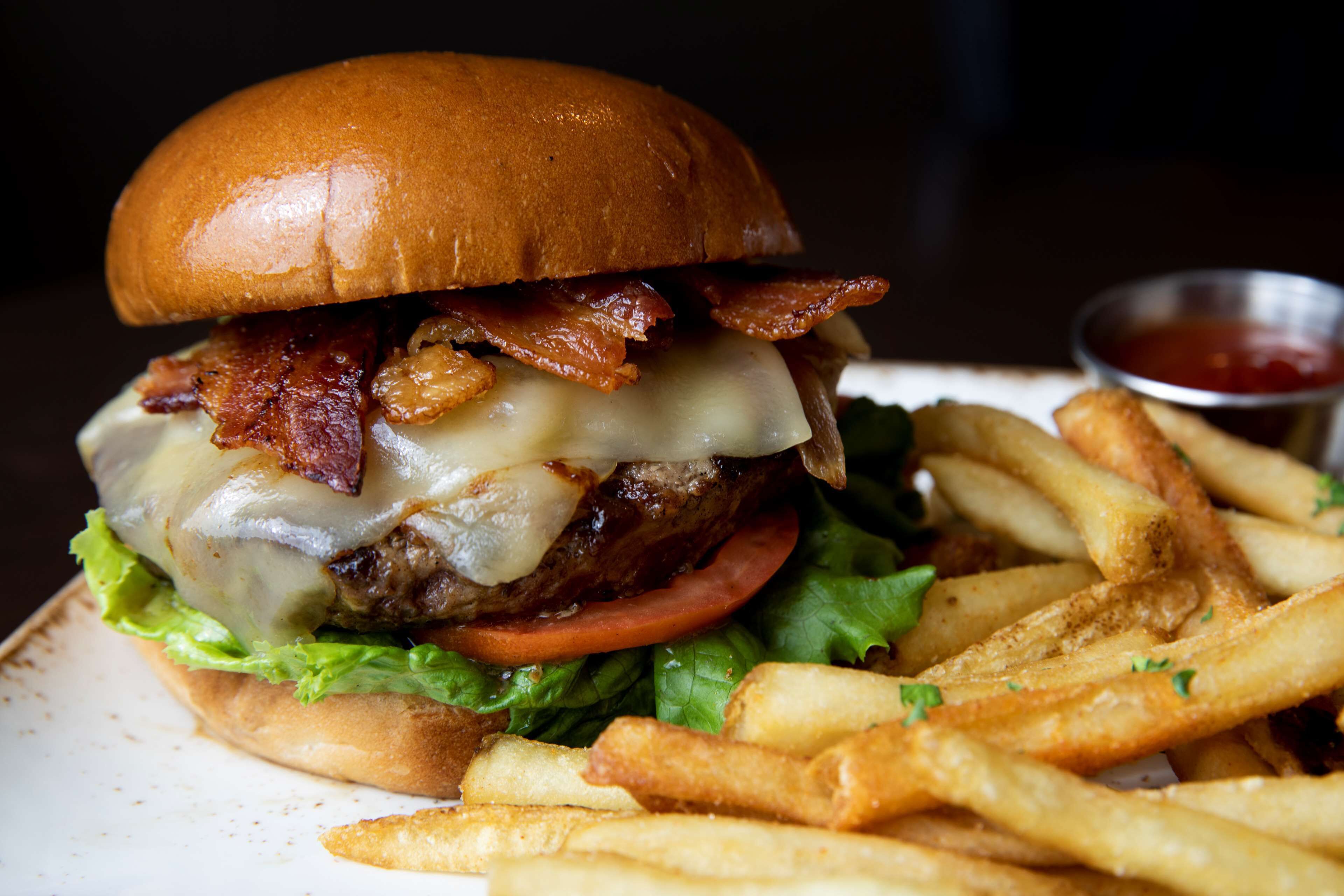 Una hamburguesa con tocino, queso y lechuga, acompañada de papas fritas y kétchup.