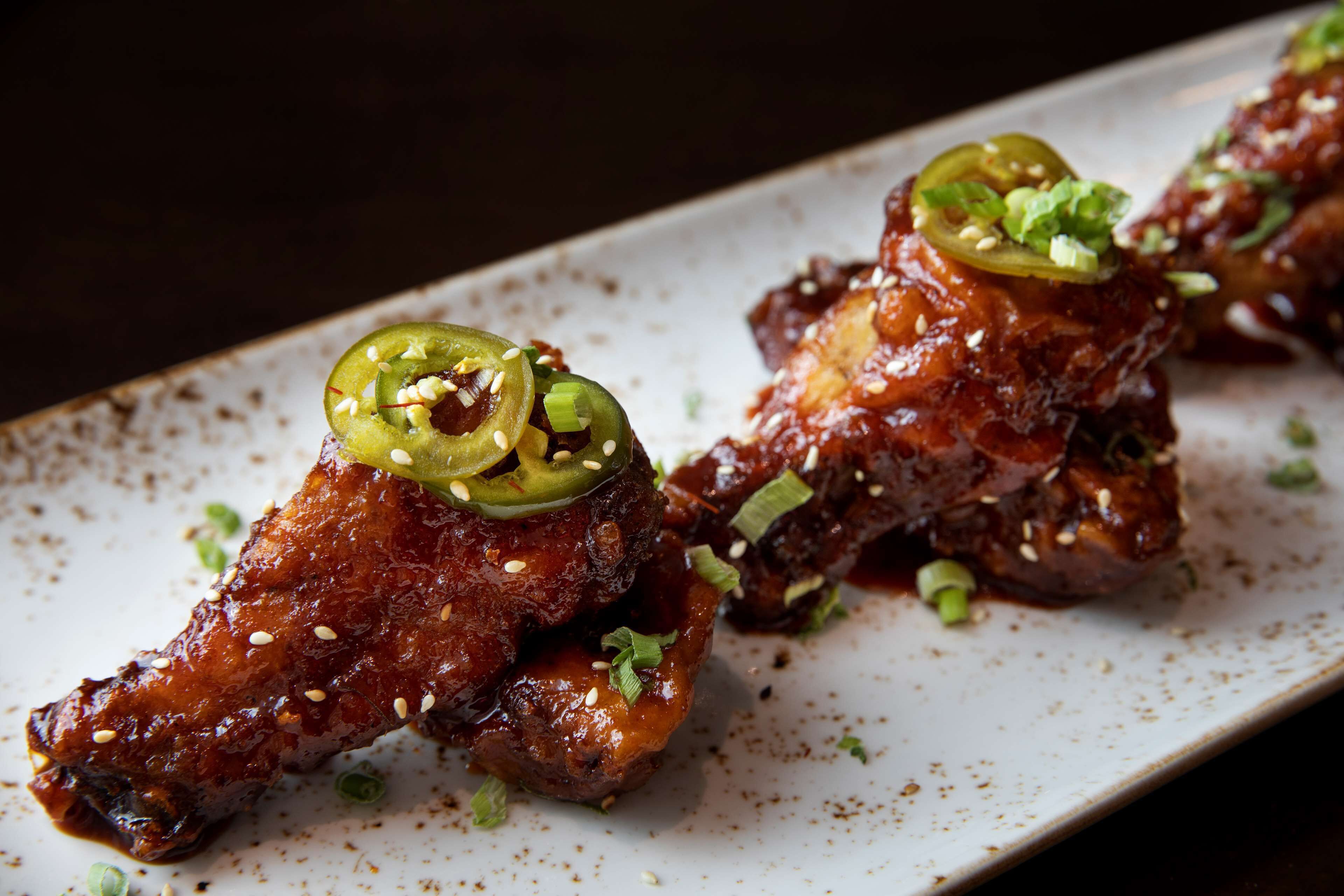 A plate of glazed chicken wings garnished with green onions and jalapeños.
