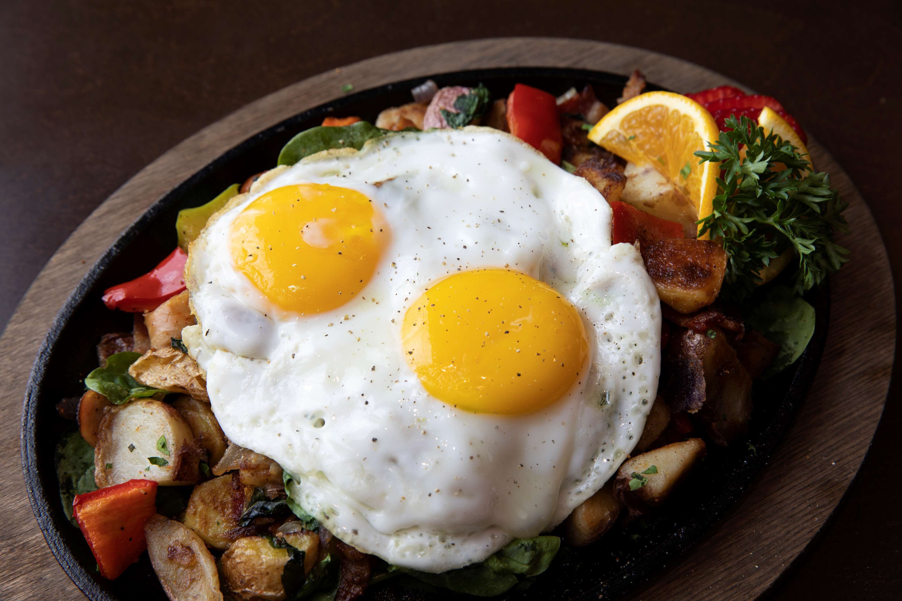 A skillet with two sunny-side-up eggs, diced potatoes, and vegetables.