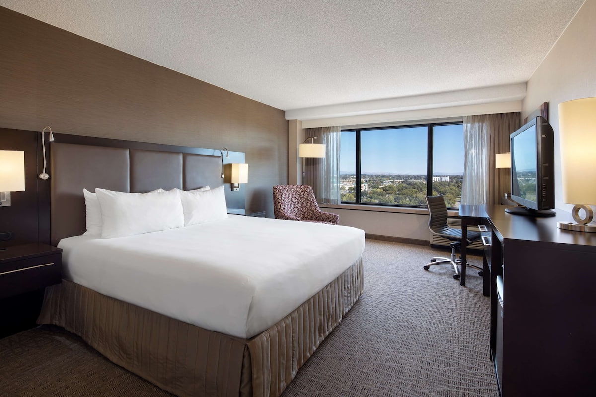 A hotel room with a large bed, a desk with a computer, a chair, and a TV.