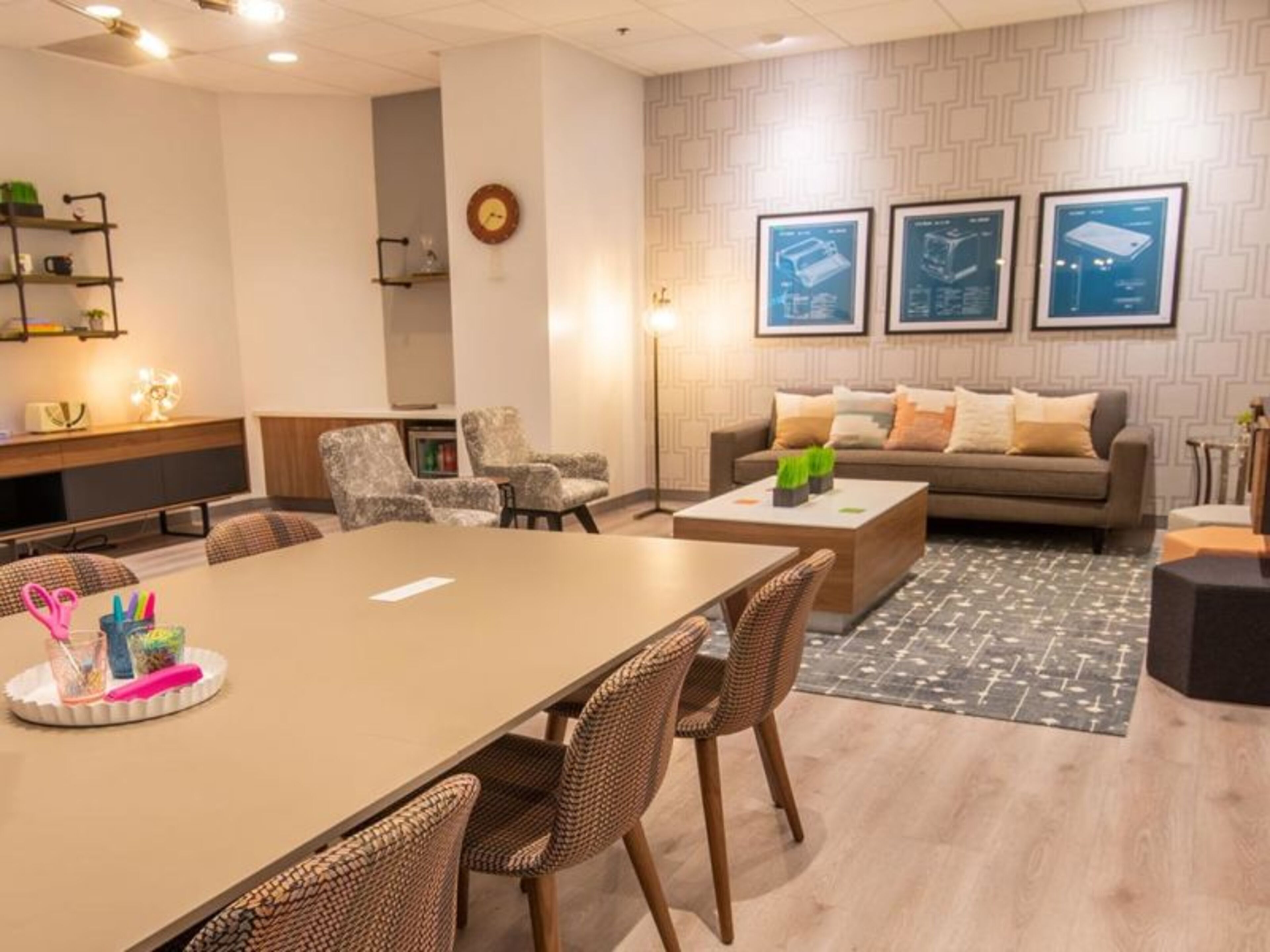 A modern meeting room with a long table, wicker chairs, a sofa, and a patterned rug.