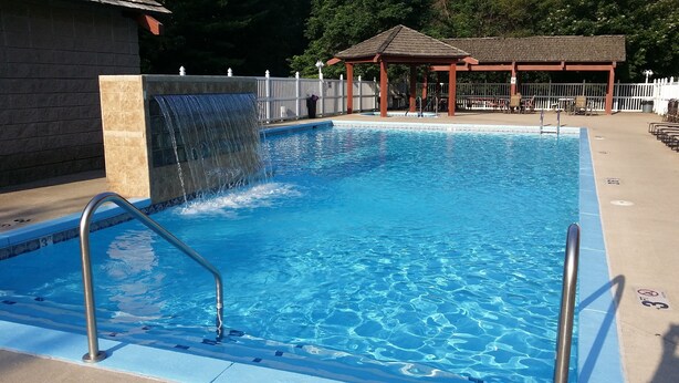 A rectangular swimming pool with a waterfall feature, a covered seating area, and a fenced deck. - Best Western Ambassador Inn & Suites (Wisconsin Dells)