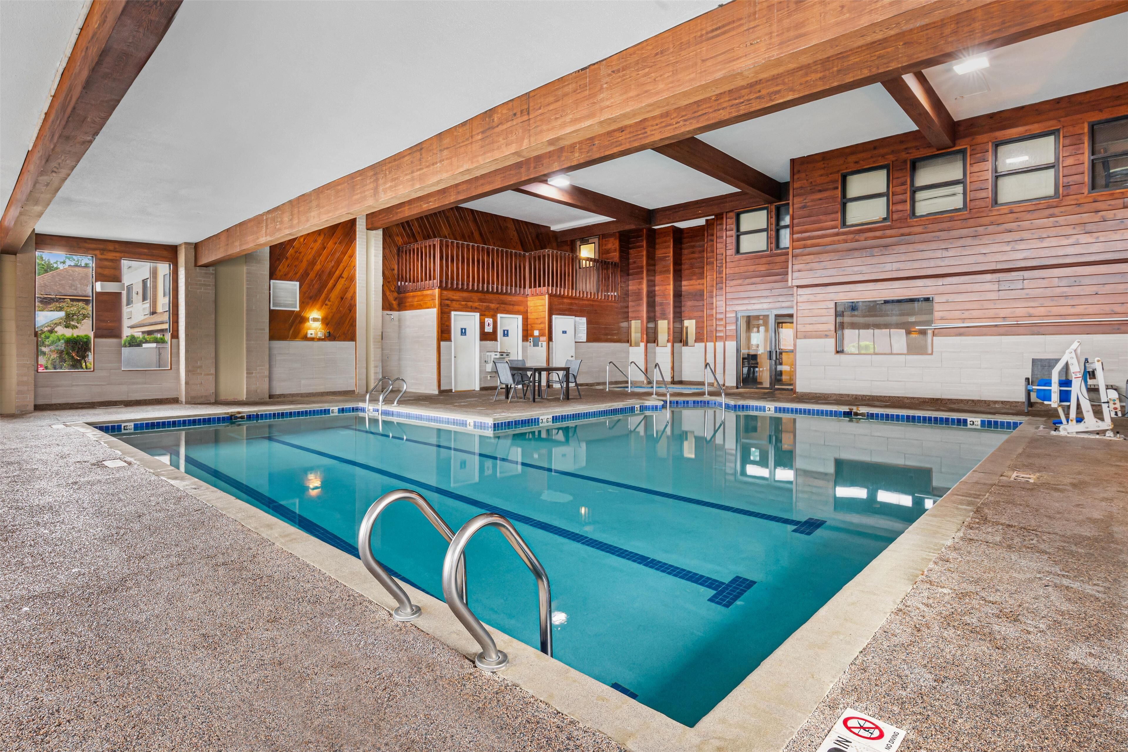 An indoor swimming pool with clear water, surrounded by a wooden deck and a tiled floor.