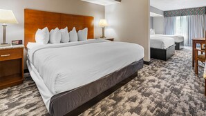 A hotel room with a large bed, two bedside tables with lamps, a small desk, and a window with curtains. - Best Western Ambassador Inn & Suites (Wisconsin Dells)