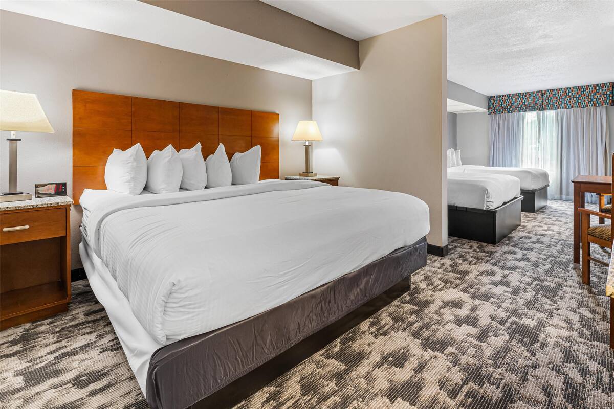 A hotel room with a large bed, two bedside tables with lamps, a small desk, and a window with curtains.