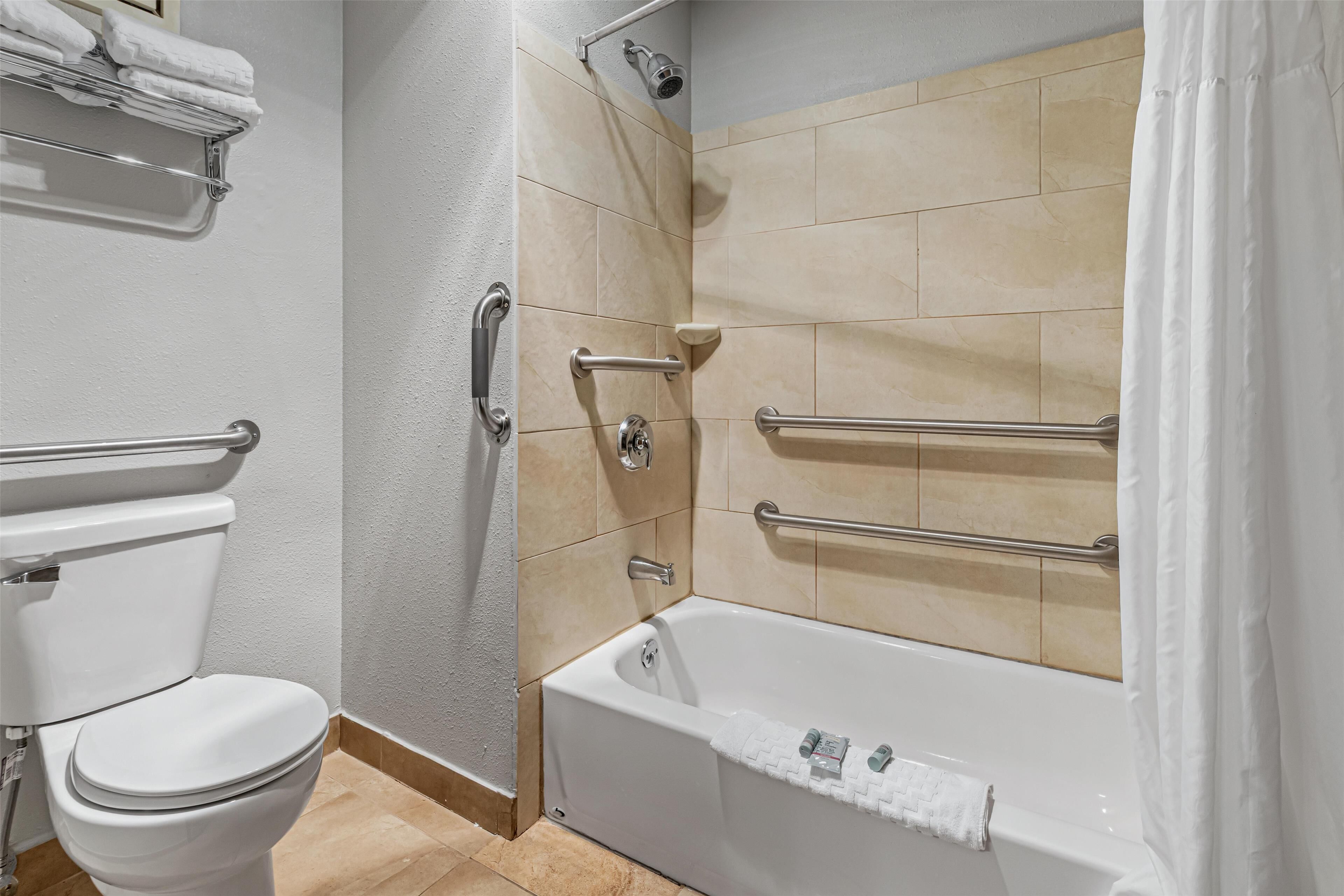 Un baño con inodoro, bañera con barras de apoyo y zona de ducha.