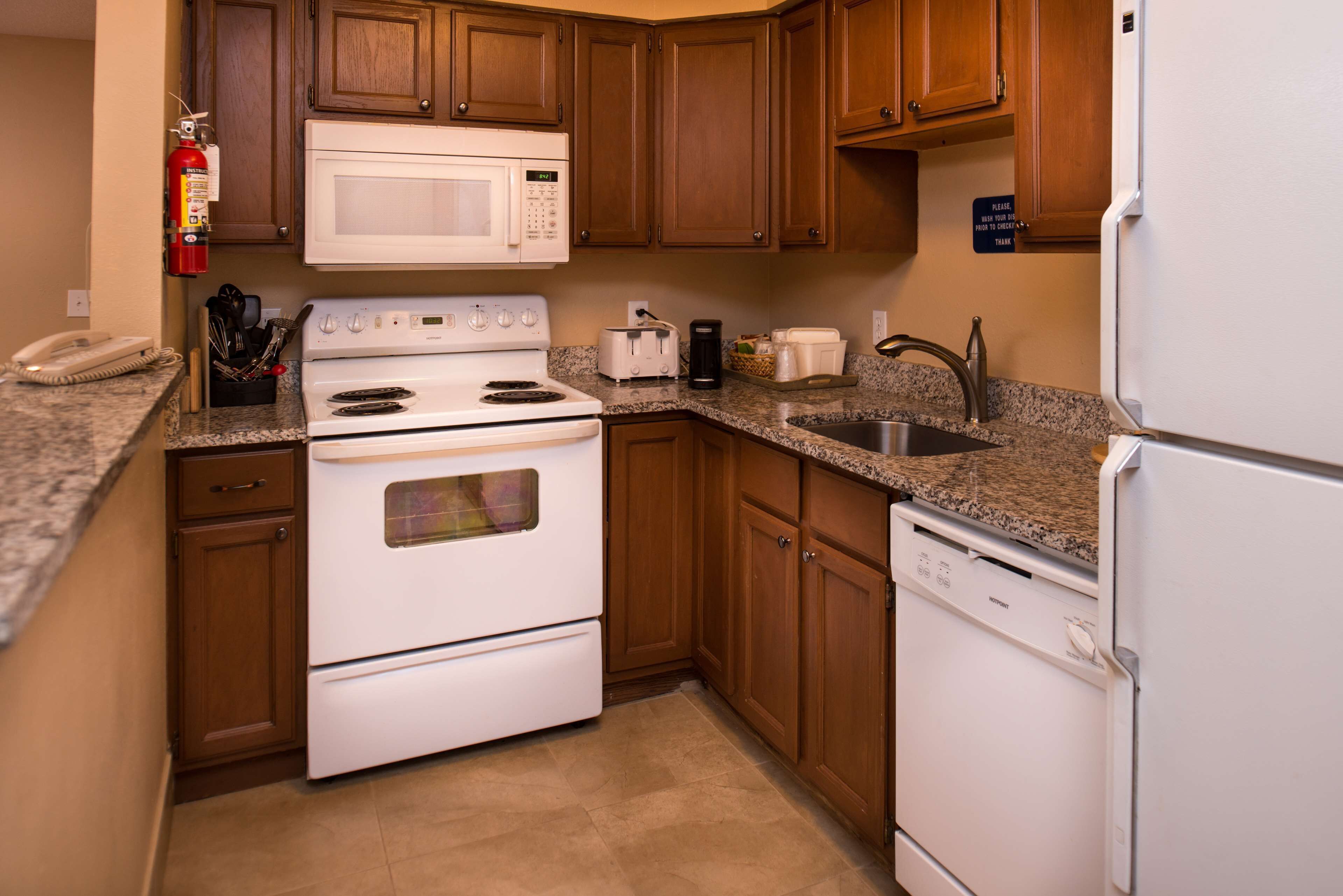 A kitchen with wooden cabinets, a white stove, a microwave, a toaster, and a sink.