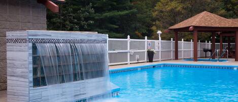 Una piscina con cascata, circondata da un recinto bianco e un gazebo.